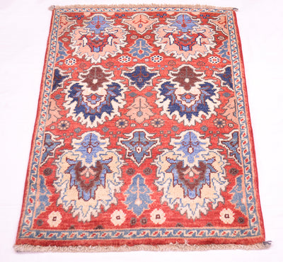 A rectangular traditional Afghan Chobi mat / small rug with a red field, featuring large central medallions in blue, beige, and brown, finished with a patterned border and fringed edges.