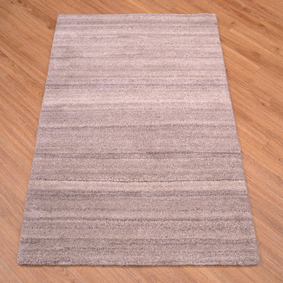 A rGrey Indian runner with horizontal textured stripes in shades of taupe, beige, and gray, shown from an overhead angle on a light brown wooden floor.