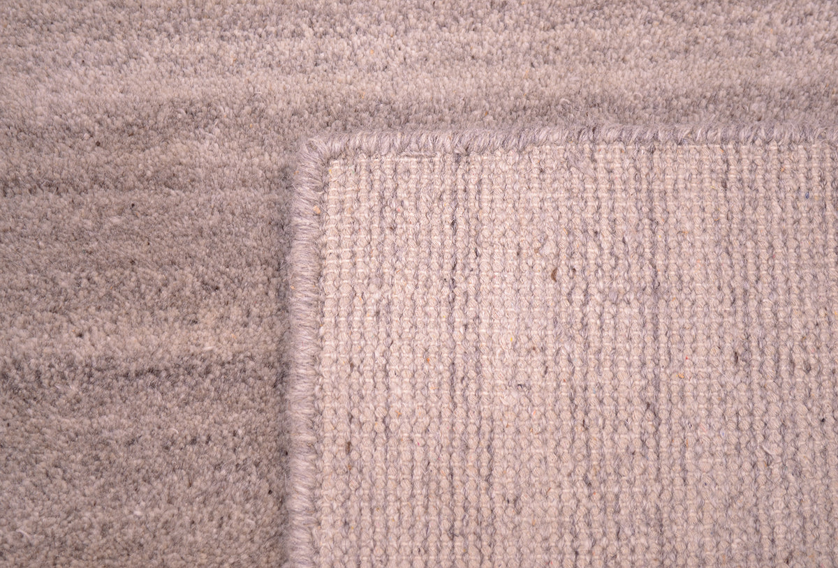 Close-up of a textured hand-knotted runner corner showing a woven pattern in a warm grey, taupe-beige colour.