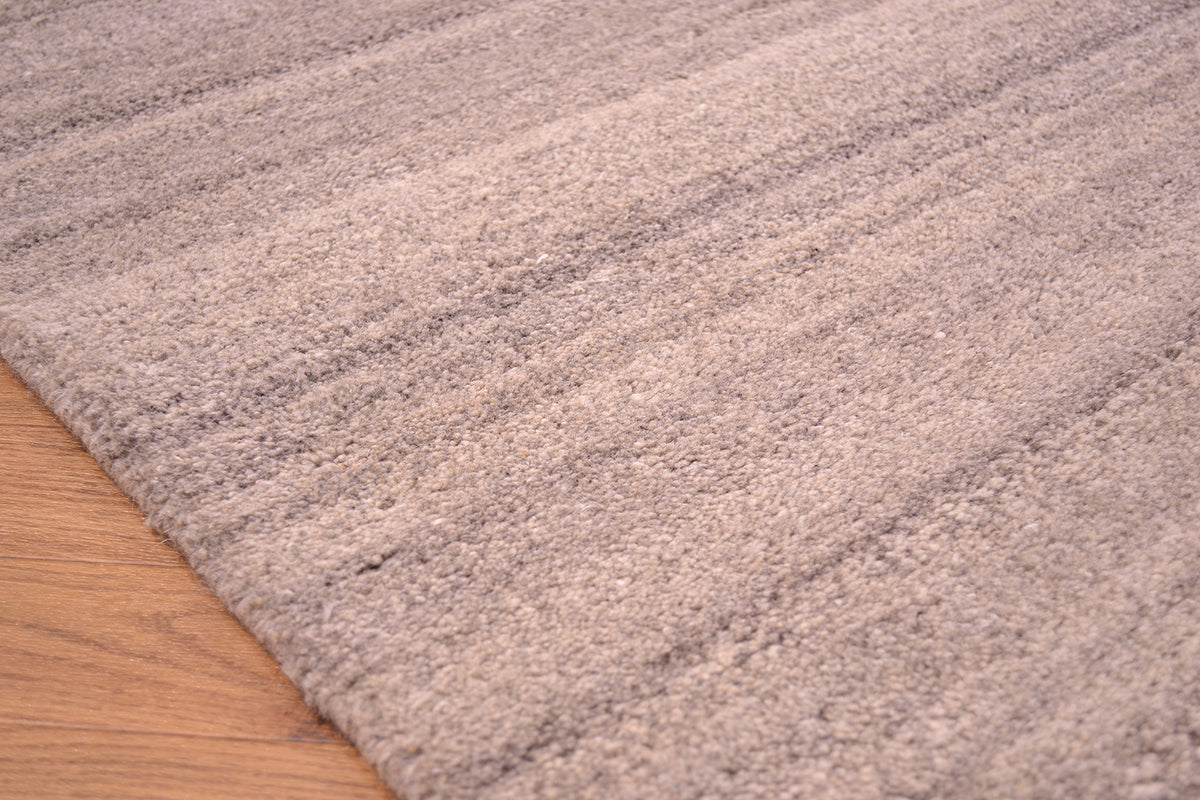 A close-up of a textured Grey Indian runner in a warm taupe-beige colour, shown laid out on a light brown wooden floor.