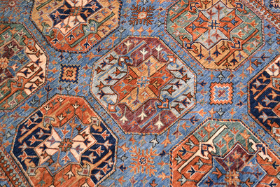 A close-up of a traditional Afghan patterned Ersari carpet featuring geometric elephant foot emblems in rust orange, navy blue, beige, and muted blue tones.
