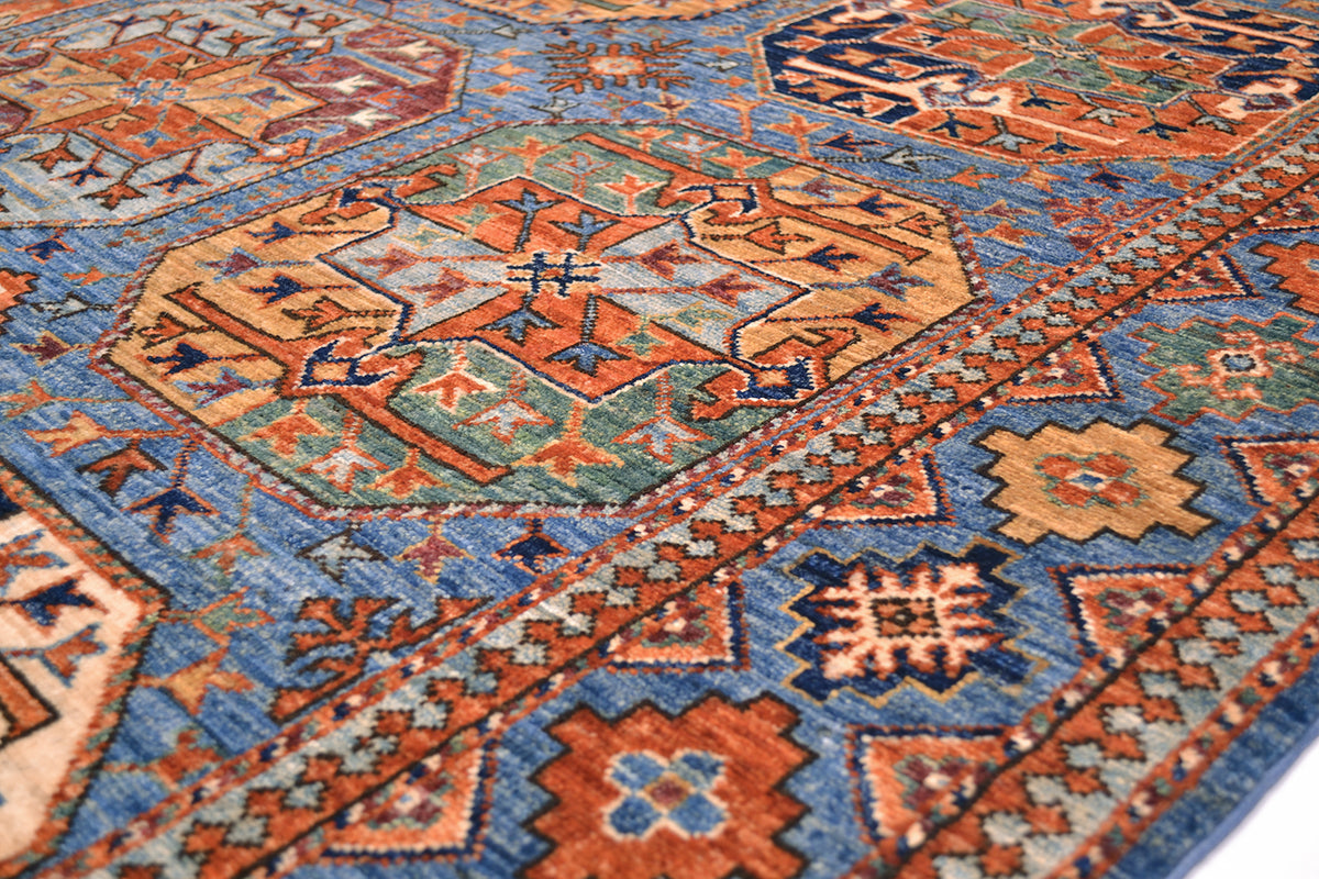 A close-up of a traditional hand-knotted patterned Afghan Ersari carpet with geometric motifs in rust orange, blue, beige, and muted green.