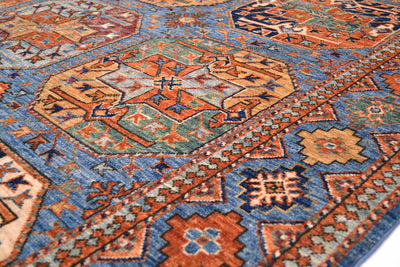 A close-up of a traditional hand-knotted patterned Afghan Ersari carpet with geometric motifs in rust orange, blue, beige, and muted green.