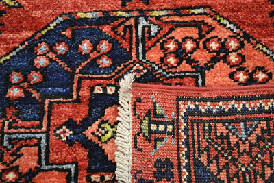Close-up of the hand-knotted back of a patterned Afgha runner with the corner turned over with a rust red base, dark blue geometric sections, and cream fringe at the corner.