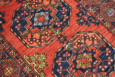 A close-up of a traditional patterned long Afghan Ersari runner rug featuring a warm red-orange field with large hexagonal medallions in navy blue, orange, yellow, and light blue.