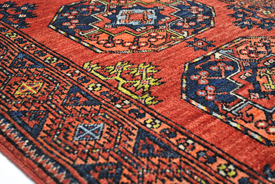 A close-up of a traditional patterned Afghan long runner rug with a warm rust-red field, dark navy geometric borders, and small yellow and light blue floral accents.