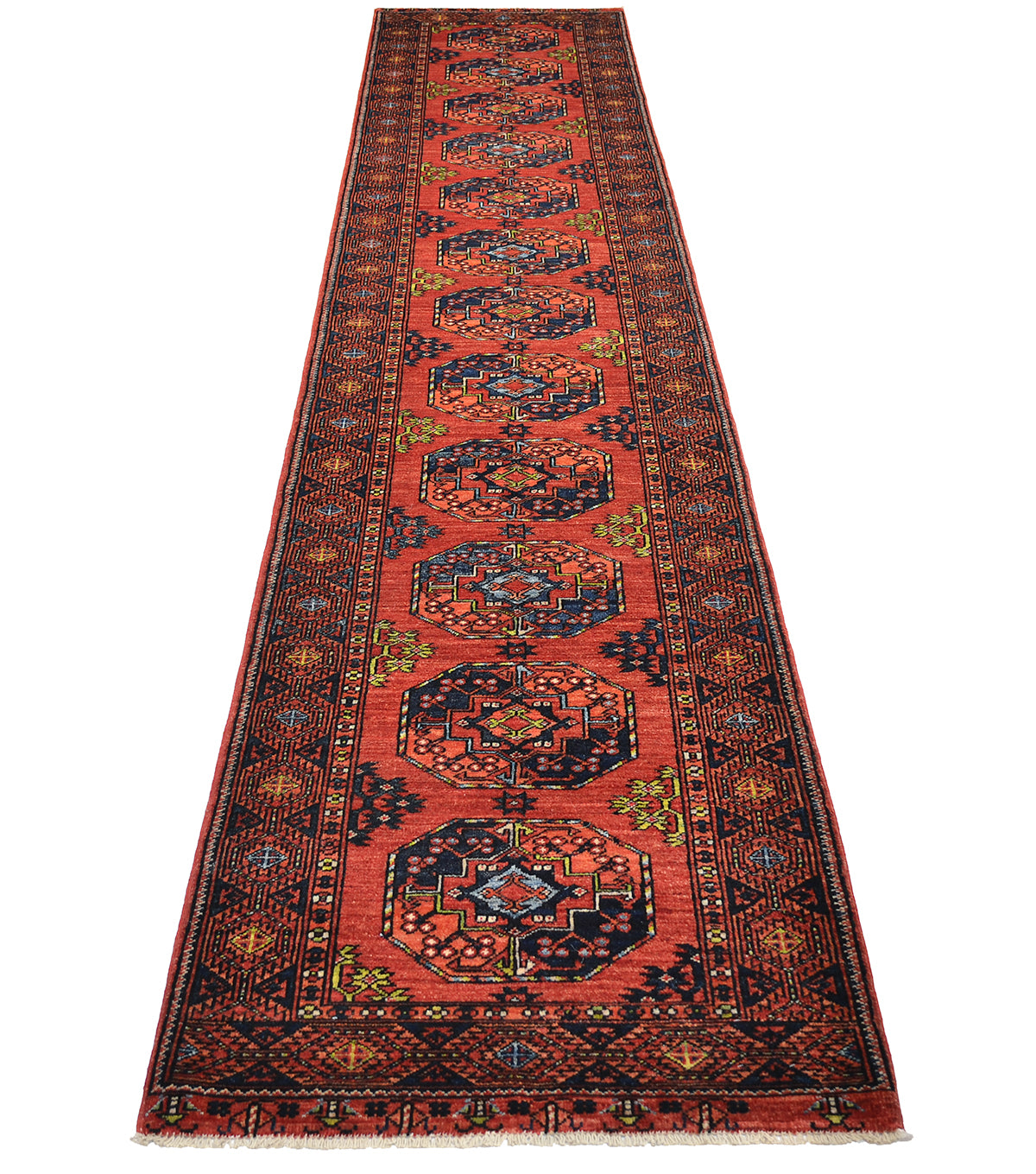 A 16' long Afghan hallway runner rug with a traditional Turkmen elephants foot design, featuring a vibrant rust field, dark navy borders, and detailed geometric guls in midnight blue, beige, orange and blue.