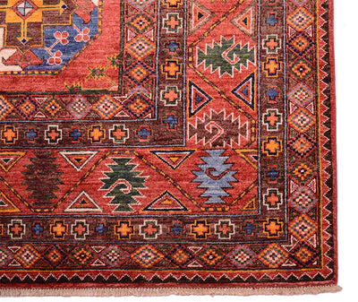 A close-up of a traditional patterned Afghan Ersari carpet corner showing a warm red-orange field with geometric borders and motifs in brown, blue, green, and cream.
