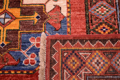 Close-up of the hand-knotted back with corner turned over of an Afghan Ersari carpet showing geometric motifs in rust red, blue, orange, brown, cream, and black, with a visible fringe edge.