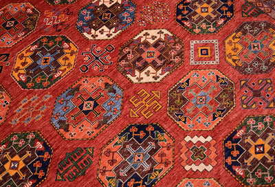 A close-up of a traditional geometric Ersari Afghan patterned carpet with a dominant rust background and multiple octagonal medallions in orange, blue, beige, and dark brown.