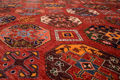 A close-up view of a traditional hand-knotted Afghan Erasri large rug with a rust field and geometric motifs in orange, blue, brown, and cream.
