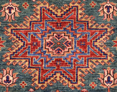 A close-up of a traditional patterned rug with a central medallion and corner motifs. The design features red, blue, and beige geometric and floral elements on a muted blue-gray background.