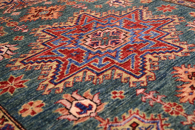 Close-up of a traditional patterned rug with a blue-green base and red, beige, and blue geometric medallion motifs.