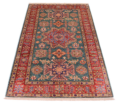 A rectangular vintage-style area rug with a complex geometric and floral pattern, featuring a teal blue center field, red borders, and cream accents, shown flat against a white background.