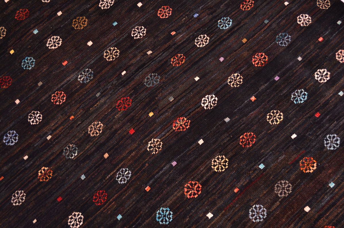 Dark brown colour with variations of shade Afghan Gabbeh rug with a repeating pattern of small multicoloured geometric and floral-like motifs in red, blue, white, and gold.