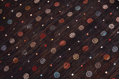 Dark brown colour with variations of shade Afghan Gabbeh rug with a repeating pattern of small multicoloured geometric and floral-like motifs in red, blue, white, and gold.