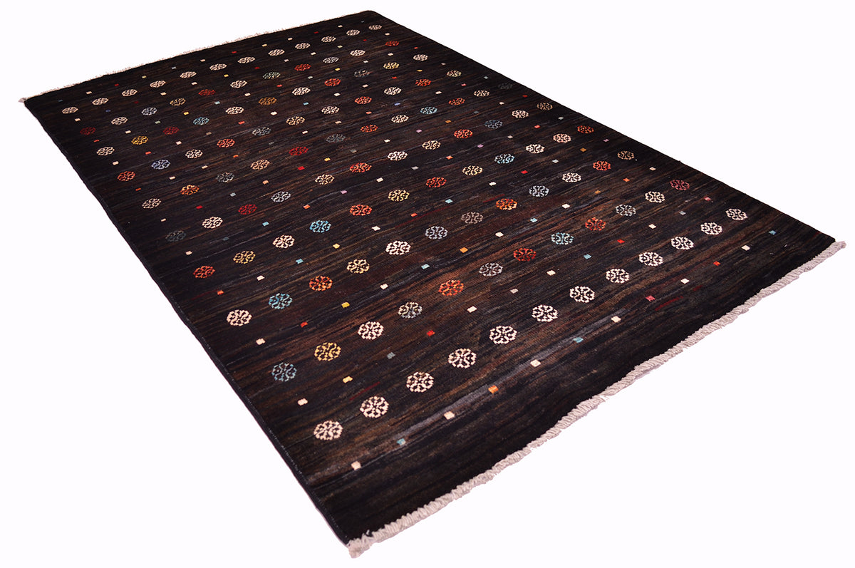 A dark brown /black handwoven Afghan Gabbeh area rug with a repeating pattern of small geometric medallions and dots in beige, orange, blue, and white, finished with a fringed edge.