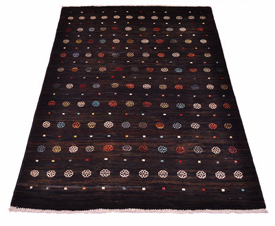 A rectangular dark brown-nearly black wool Afghan Gabbeh area rug with a woven geometric pattern of small circles, dots, and floral-like motifs in beige, red, blue, and white, finished with a light pink fringe.
