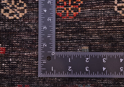 Close-up of a dark patterned Handmade Afghan Gabbeh rug with a metal L-square ruler placed over it to show scale of the knot density, highlighting the woven texture and colour details.