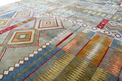 A close-up view of a large size handmade Gabbeh carpet with a geometric tribal pattern in muted tones of blue, beige, rust orange, and red.