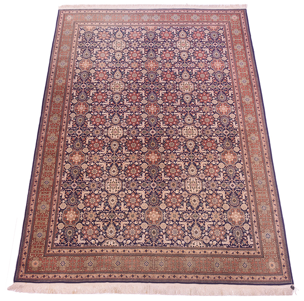 A rectangular Hereke area rug with an intricate floral and geometric pattern, featuring a dark navy blue field, rust red borders, and cream accents, finished with white fringe on the ends.