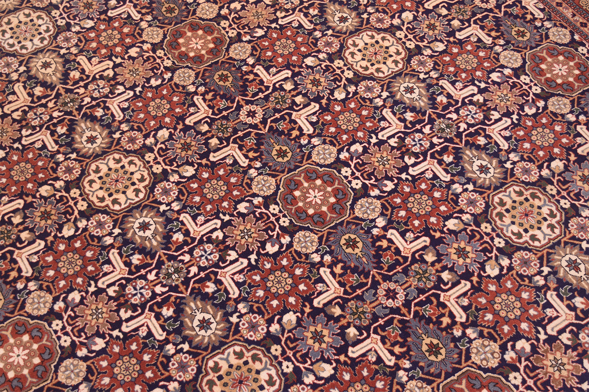 A close-up of an intricate Wool Hereke rug featuring a dense floral and geometric pattern in deep red, beige, navy blue, and brown tones.