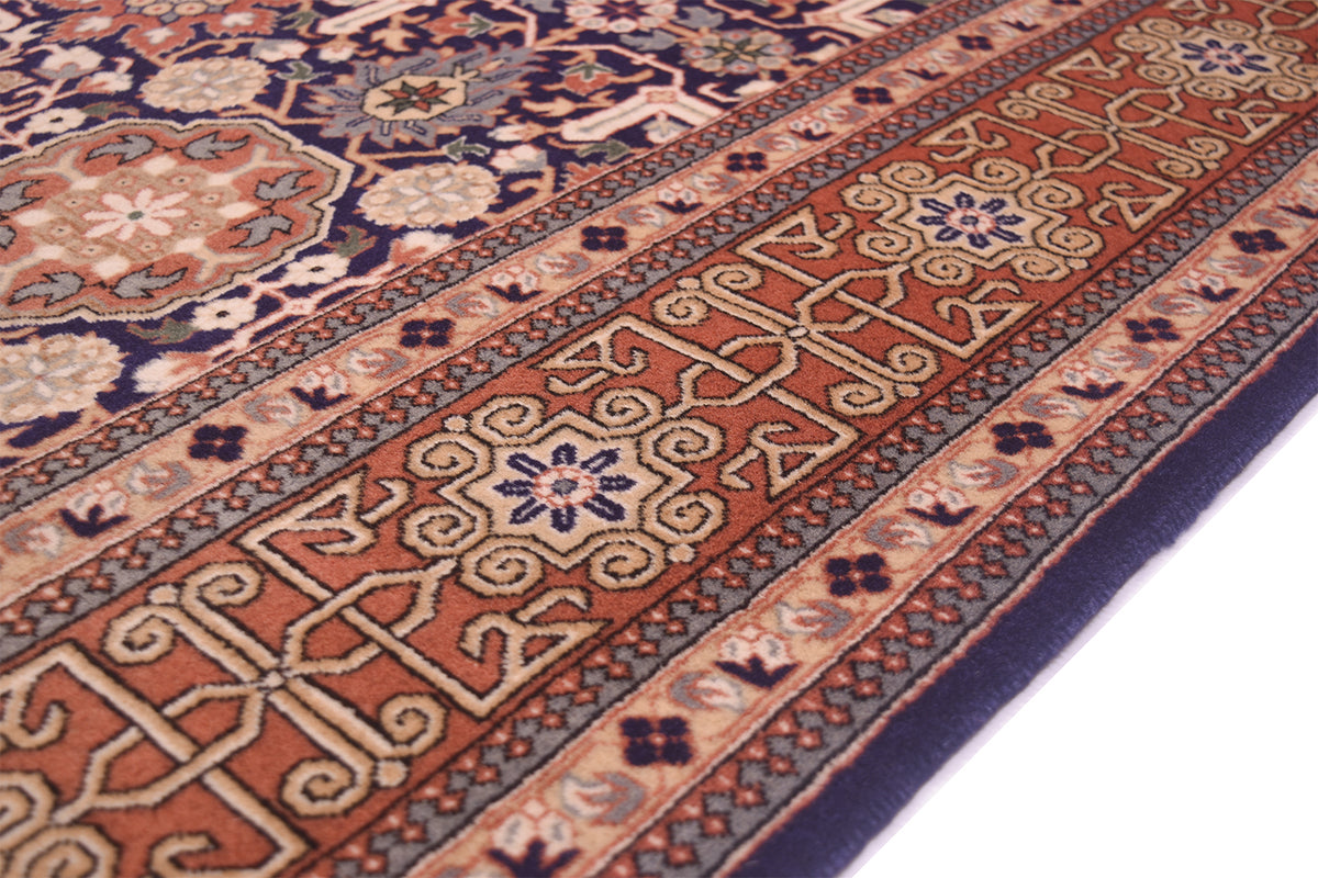 A close-up of a traditional Hereke rug showing border detailing woven motifs on a prominent rust-red border with beige and a navy blue field.