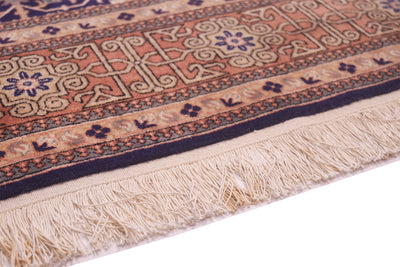 Close-up of a patterned Hereke rug border showing cream fringe, a peach and beige central field, and dark navy and blue geometric and floral borders. 