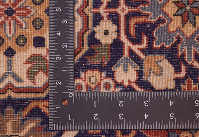 Close-up of the back of a Hereke rug corner with a dark metal ruler placed to show scale, featuring a beige, navy, red, and green ornamental design.