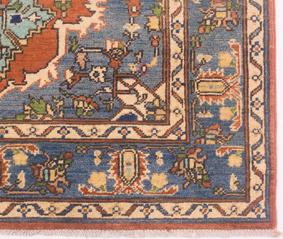 Close-up of an ornate Afghan Heriz area rug corner showing a blue field with cream, rust, and green geometric and floral motifs, plus a patterned border and fringe.