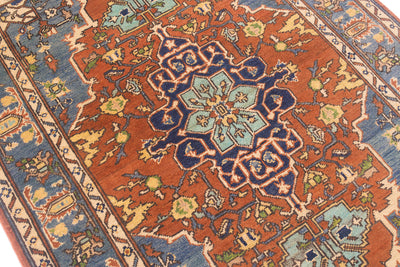 A close-up of a traditional oriental Afghan wool rug featuring a rust-orange field, a central blue and teal medallion, and blue floral borders.