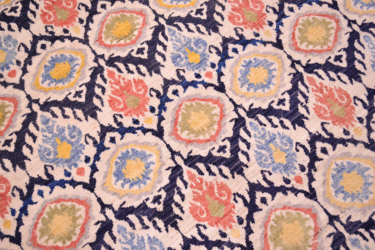Close up detail of field of handwoven pile of ikat design carpet with dark navy blue background, cream, light grey outlining, light blue, light terracotta, gold yellow and olivey green.