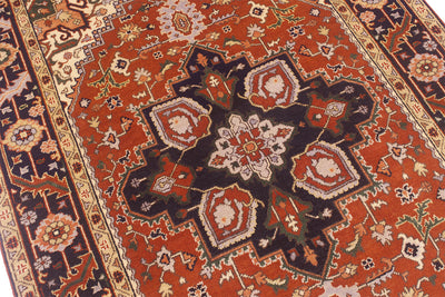 A close-up view of a traditional Handmade Indo Heriz carpet with a warm rust-red field, dark navy medallion, and cream floral details.