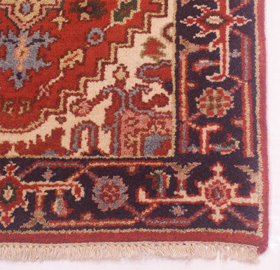 A close-up of an ornate Handmade extra long Indo Heriz runner corner showing a red field, cream and beige motifs, dark navy borders, and fringed edges.