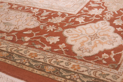 Close-up of an ornate area rug with a rust red field, cream floral medallion, and detailed beige, olive green, and orange border patterns.