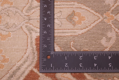 A close-up of the back of a patterned rug in beige, tan, and muted orange tones, shown with a black metal ruler to indicate scale.