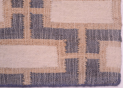 Close-up of a woven textile pattern with alternating cream and slate blue-gray geometric blocks separated by tan lines.