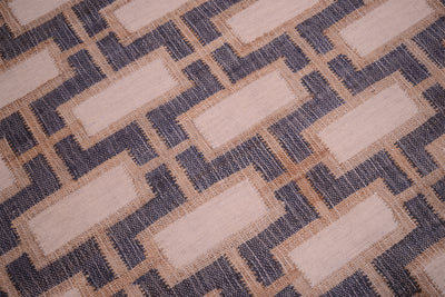 A close-up of a woven rug or textile with a geometric pattern of beige rectangles outlined in tan, separated by dark navy zigzag lines.