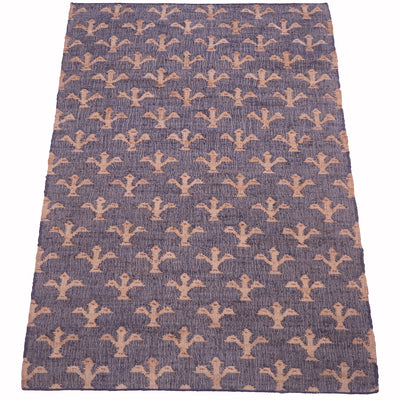 A rectangular area rug with a textured, woven surface featuring a repeating pattern of stylized fleur-de-lis motifs in a muted peach-beige color on a dusty blue-gray background.
