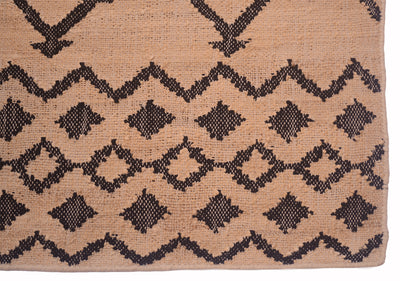 A close-up of a woven textile with a tan background and a dark brown geometric pattern of zigzags and diamonds.