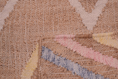 Close-up of a woven rug with a textured beige base and geometric patterns in pink, blue, yellow, and cream.