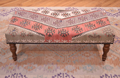 Vintage Kilim Bench with geometric kilim upholstery in soft terracottas. creams, light greens. soft greys and beige natural cream and chestnut brown stylized hooked mini medallions and motifs.  Dark borwn wooden legs. and beaded edging. Kilimbench resting on a soft wash Afghan kilim with muted colours.
