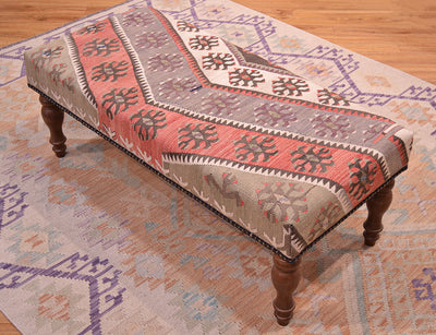 View of vintage Anatolian kilim in soft greens, beige and terracottas with beige/cream detailing.    Resting on a sfot ws afghan kilim and wooden floor. Dark wooden legs. Vintage turkish kilim used for upholster kilim bench.
