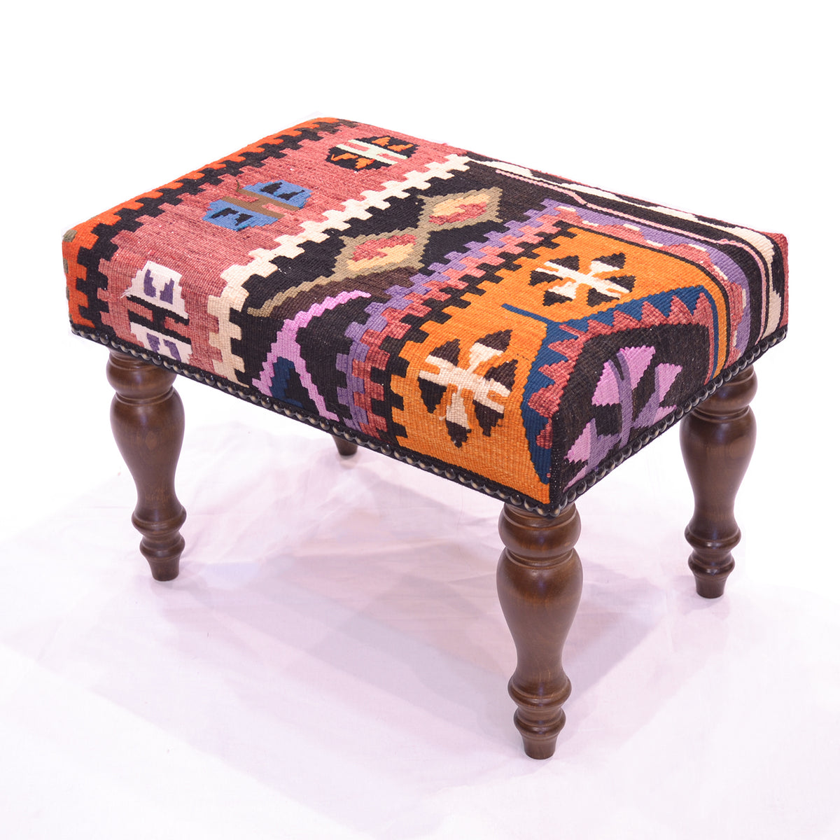 Multi-colour Anatolian Kilim Footstool with rust, orange, mauve, blue and chestnut brown with white highlights with brwon wooden legs on a white backgrounsd