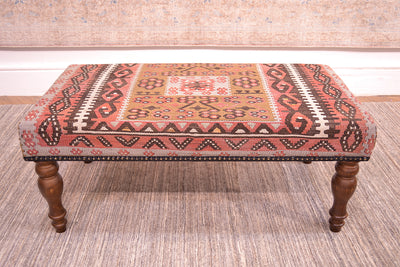 Side view of anatolian kilim long bench  with geometric design with rose terracotta, cream, soft brown and blue grey with centralised floral geometric medallion with a light olive green. Placed on a afghan neutral handmade rug.