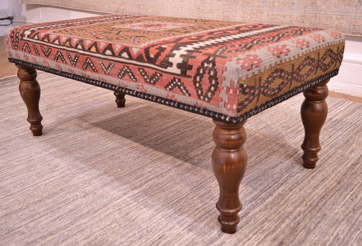 Close up detail of corner and wooden leg of long bench seat upholstered with vintage turkish kilim. With wooden legs and soft colours of light olive green, light grey-blue and soft rose terracottas.