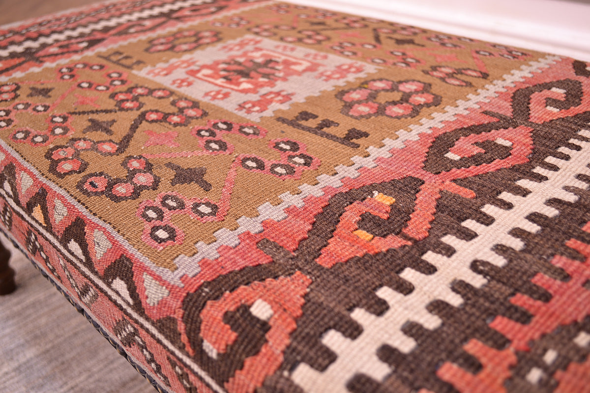 Close up detail of  vintage kilim upholstered bench seating. With pure wool killim with terracotta, and light olive green centralised square motif. Hints of golden yellow/orange. Stylized florettes hooked designs and crenelllations.