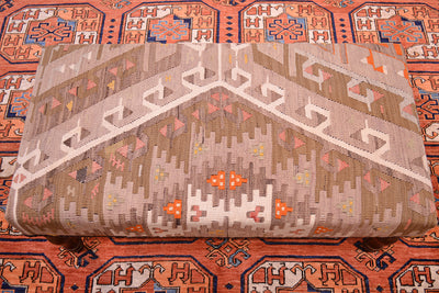 View of geometric patterning of kilim bench stool with muted softened pastel tones of vintage turkish kilim. Place on a terracotta afghan carpet.