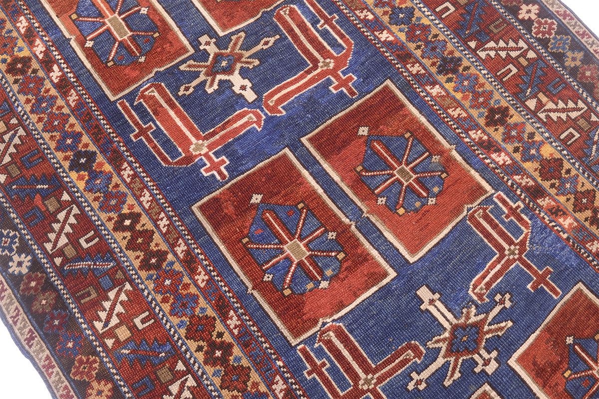 A close-up of a traditional antique Caucasian Karagashli rug with a deep blue field, red rectangular medallions, and cream geometric motifs.