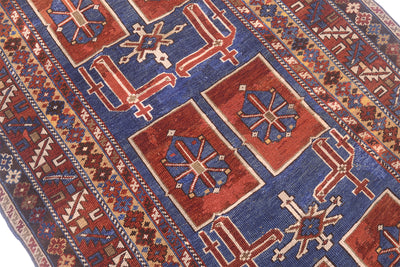 A close-up of a traditional antique Caucasian Karagashli rug with a deep blue field, red rectangular medallions, and cream geometric motifs.